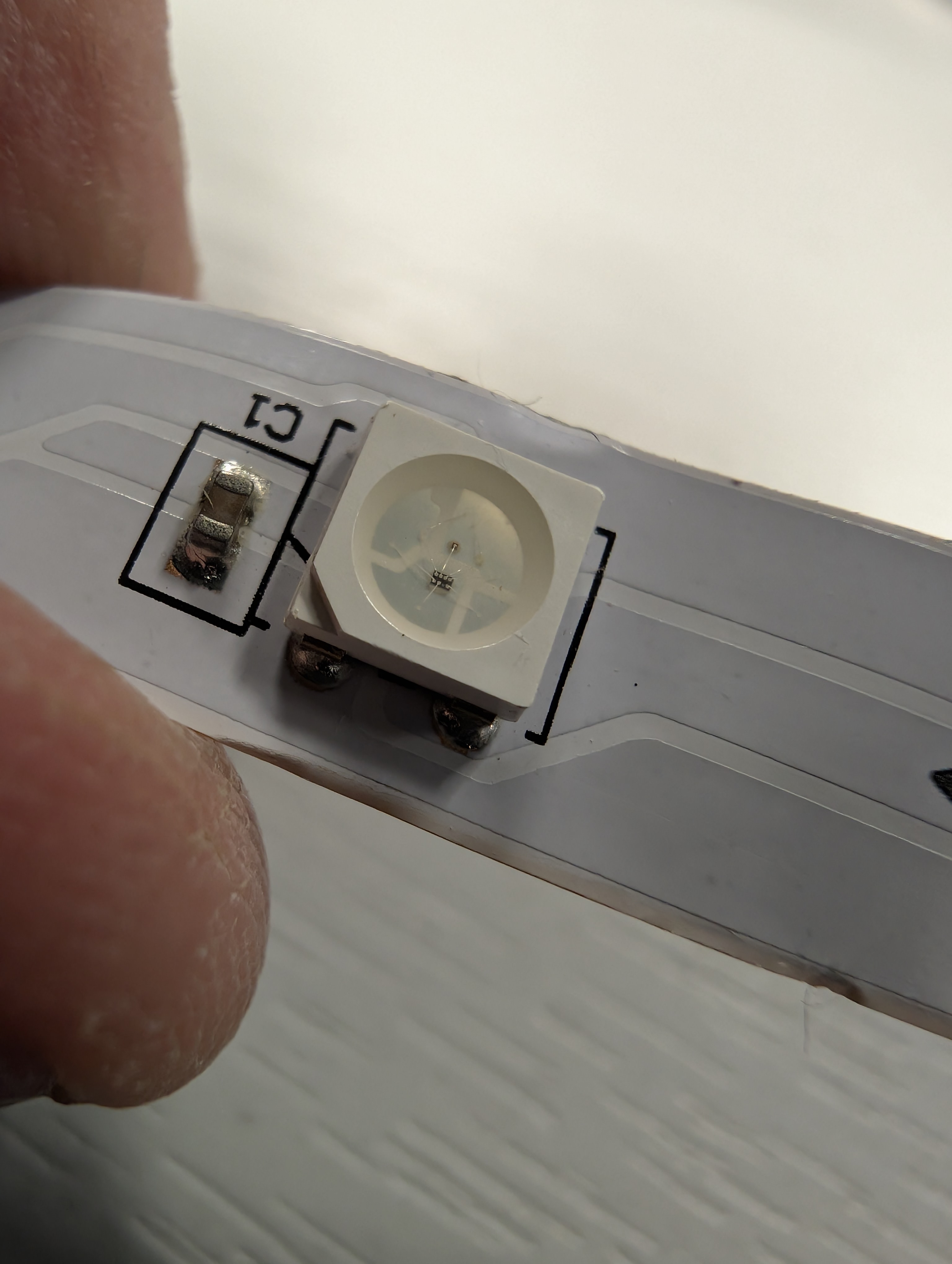 Close-up of a WS2812B LED on a flexible strip showing the controller IC inside the package and the C1 decoupling capacitor